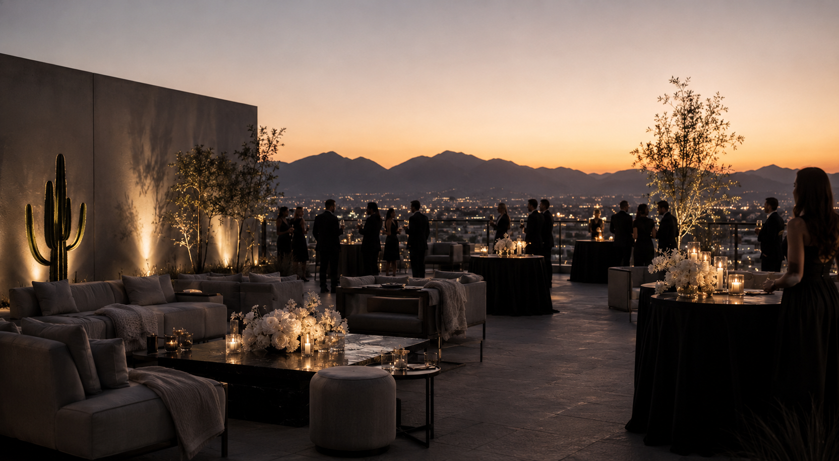 Rooftop social gathering at sunset with lounge seating, white florals, and mountain views.