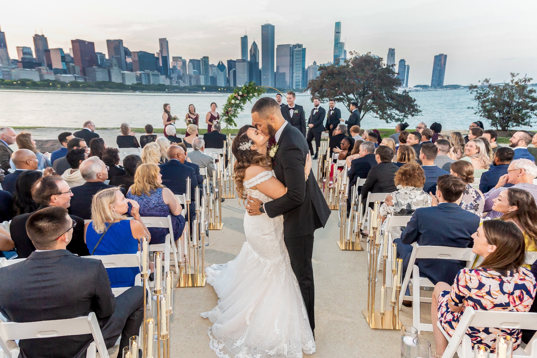 Bride and groom sharing a kiss at a waterfront wedding ceremony with the skyline behind them.